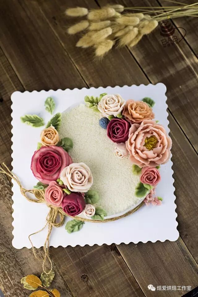 White floral cake with buttercream roses and a peony on a scalloped square board